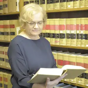 A woman reads a thick law book in front of shelves of law books.
