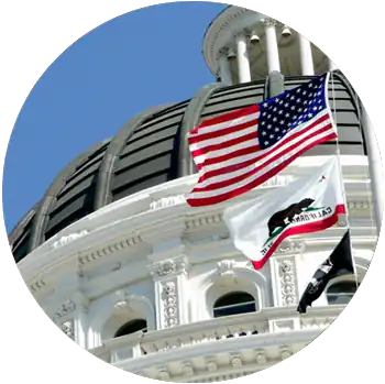 The American flag and State of California flag are raised in front of the Sacramento State Capitol.